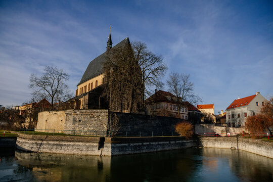 City fortifications and pond with water near gothic church of Saint Gothard with bell towers in center of medieval town Slany in sunny winter day, Central Bohemia, Czech Republic