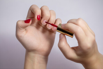 A little girl paints her nails with red varnish.