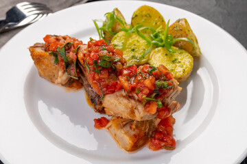 stewed pieces of meat with spices. With baked new potatoes and tomato salsa sauce on a white platter and dark background. Dish for the restaurant menu