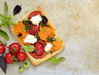 Puff pastry tomato tart with cottage cheese, pesto and basil, top view, copy space