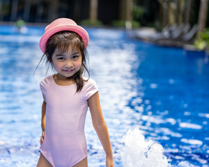 Portrait of pretty asian child smilling and posing on swimming pool background wearing pink swim suit and pink summer hat