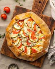 Homemade savory galette with vegetables, wheat pie with tomatoes, zucchini, blue cheese Gorgonzola. Rustic crust crostata on dark linen textile tablecloth. Vertical