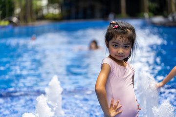 Portrait of pretty asian child smilling and posing on swimming pool background wearing pink swim suit