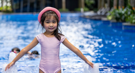 Portrait of pretty asian child smilling and posing on swimming pool background wearing pink swim suit and pink summer hat