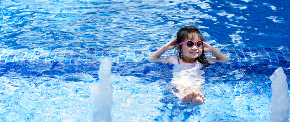 Portrait of pretty asian child smilling and posing on swimming pool background wearing pink swim suit and sun glasses