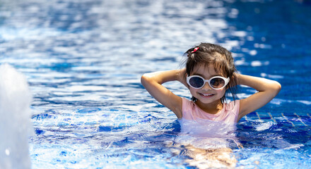 Portrait of pretty asian child smilling and posing on swimming pool background wearing pink swim suit and sun glasses