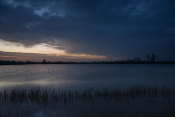 Dark evening clouds at the lake with reeds