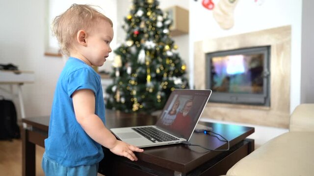 Little boy staying home in lockdown on Christmas holidays and video calling grandma and grandpa. Little grandson has video call with grandparents, kid kissing screen, funny video