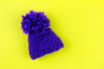 Purple knitted hat with pompom on yellow background