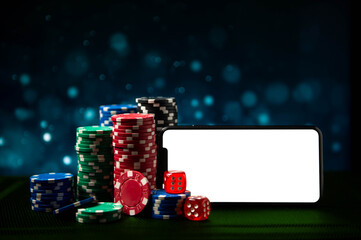 Casino. Online casino. Game chips and dice lie on a table next to a smartphone against a blurred dramatic background. Online poker. Free space. Game chips for betting in gambling. Dice. Poker chips.