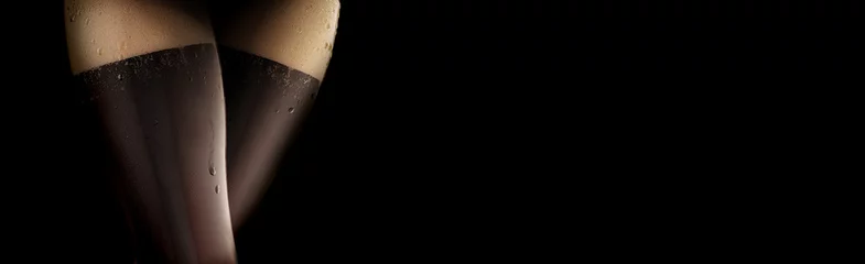 Two glasses of Dark beer reminiscent of a cool sexy female legs in black stockings. Black background.For advertising beer or alcoholic to a bar or party. Copy space © Vladimir Razgulyaev