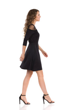 Side View Of Walking Young Woman In Elegant Black Dress And High Heels.
