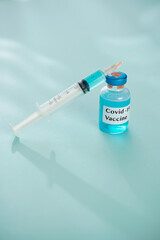 Small vial with blue vaccine against covid-19 and syringe on table in medical office, disease treatment concept