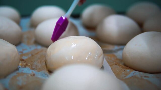 Close-Up of fresh Hamburger Buns, dough. bakery products. production and cooking. Silicone and plastic brush with an egg. Woman hands
