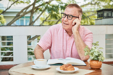 Fototapeta na wymiar Portrait of senior man in glasses eating breakfast and writing his thoughts and plans in journal in the morning