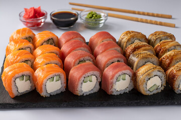 Asian food with sushi set of salmon, tuna and eel with philadelphia cheese on on a slate board on a white background. Served with soy sauce, wasabi and pickled ginger. Closeup.