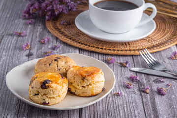 Traditional British scones and a cookie on a plate with a white coffee cup on a wooden table with a flower blurred background. Close-up photo with copy space for text