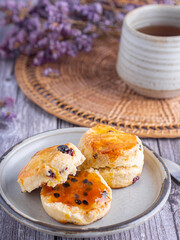 Traditional British scones on a plate with a teacup on a wooden table with a purple flower blurred background
