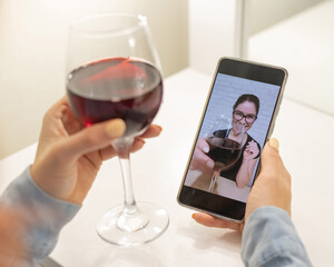 The women talk over video communication on the phone and drink red wine. The quarantined girl is not making a video call