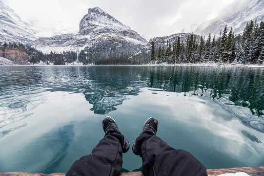 Legs of traveler relaxing on pier with rocky mountains reflection in Lake O'hara on winter at Yoho National Park