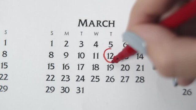 Female hand circle day in calendar date with a red marker. Business Basics Wall Calendar Planner and Organizer. MARCH 12th