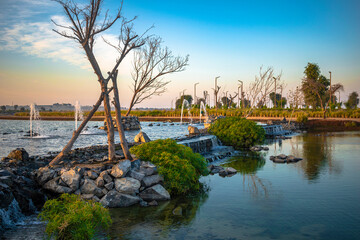 An artificial lake in the middle of the desert in UAE. Beautiful view of man-made lake and blue sky with green nature and water fountains.