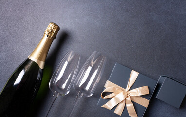 A bottle of champagne, two glasses, a gift box. On a black background. Flat lay.