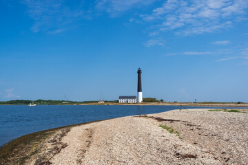 Fototapeta na wymiar View to the beach of Sõrve peninsula cape with sand and pebbles by coastline. Lighthouse in the background. Focus on water and pebbles in foreground 