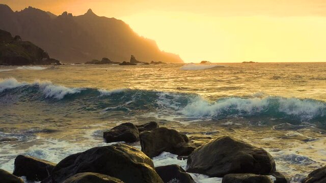 Ocean waves crash on rocks and spray in beautiful sunset light near Playa de Benijo beach in Tenerife Canary Islands
