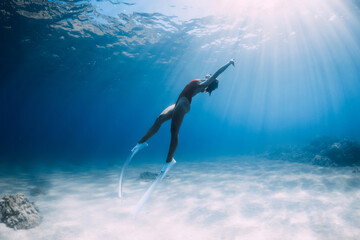 Freediver girl glides over sandy sea with white fins. Freediving with attractive woman in clear ocean