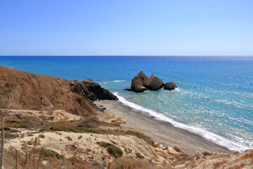 Fototapeta na wymiar Aphrodite Beach with Stone Rocks in Aphrodite bay of Mediterranean sea water, blue sky in sunny day background, Petra tu Romiou, Cyprus