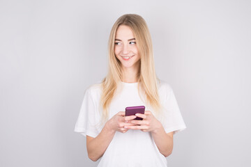 Photo of cheerful cute beautiful young woman chatting by mobile phone isolated over white wall. Looking aside to copyspace.