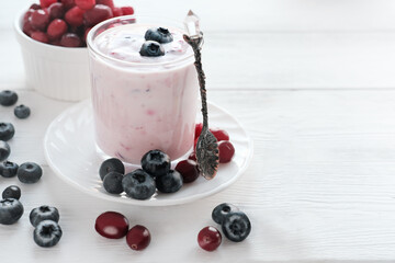 homemade yogurt with berries in a glass. blueberries and cranberries on a white table near the...