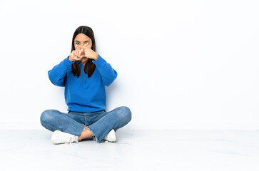 Young mixed race woman sitting on the floor isolated on white background making stop gesture with her hand to stop an act
