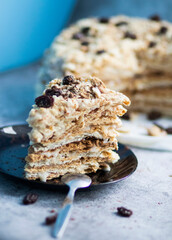 Napolion cake. A piece of cake on a black plate, decorated with raisins. Stands on a table with a gray background