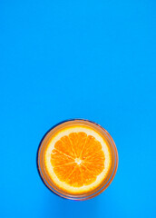 Cut orange on the surface of orange juice in a glass on a blue background.