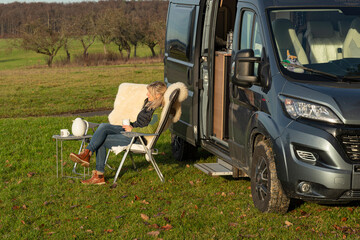 Frau sitzt vor Wohnmobil und liest ein Buch 