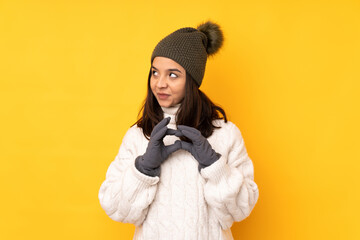 Young woman with winter hat over isolated yellow background scheming something