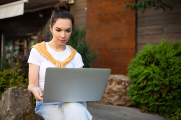 woman student studying on the street sitting with a laptop on her lap