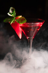 an alcoholic cocktail with red ice is shrouded in smoke from a hookah