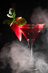 an alcoholic cocktail with red ice is shrouded in smoke from a hookah