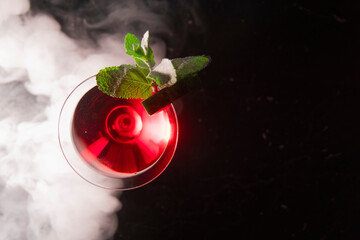 an alcoholic cocktail with red ice is shrouded in smoke from a hookah