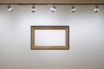 Empty wooden frame on the white wall with spot lights at art gallery