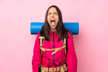 Young mountaineer girl with a big backpack over isolated pink background shouting to the front with...