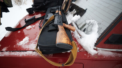 Kalashnikov assault rifle on a case against the background of a red car in the winter