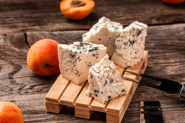 Dorblu cheese pieces with peaches fruit on a wooden background, Danish blue cheese, Food recipe background. Close up.
