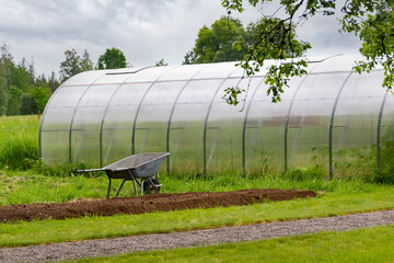 Plant nursery of organic vegetable surrounded by nature and trees with sky and coulds, greenhouse garden bed wheelbarrow