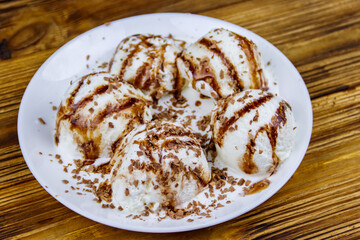 Vanilla ice cream with chocolate topping in white plate on a wooden table