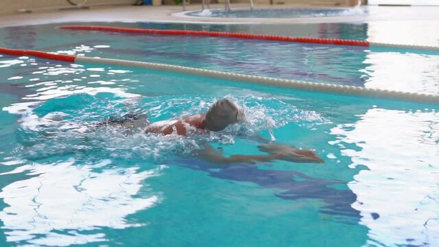 A man in a gray cap and goggles swimming breaststroke