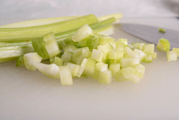 Green Celery Being Sliced on White Cutting Board With Chef's Knif and Wood Stand